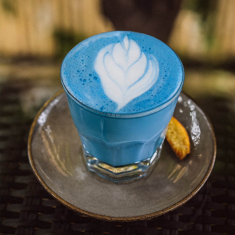 Verre de latte au blue matcha crémeux, vu de dessus, avec un motif en latte art blanc, posé sur une tasse bleue