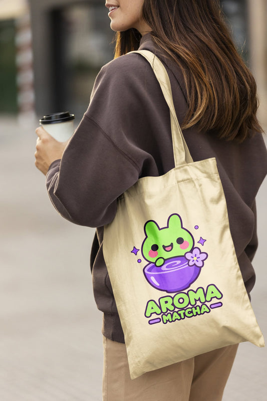 Femme portant un tote bag en coton écru Aroma Matcha, illustré d'un petit lapin vert kawaii dans un bol violet, avec le logo de la marque.