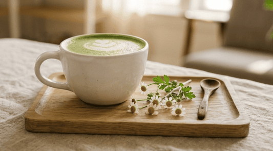 Grande tasse en céramique blanche de matcha latte avec latte art posée sur un plateau en bois, entourée de fleurs de camomille et d'une cuillère en bois, lumière dorée naturelle