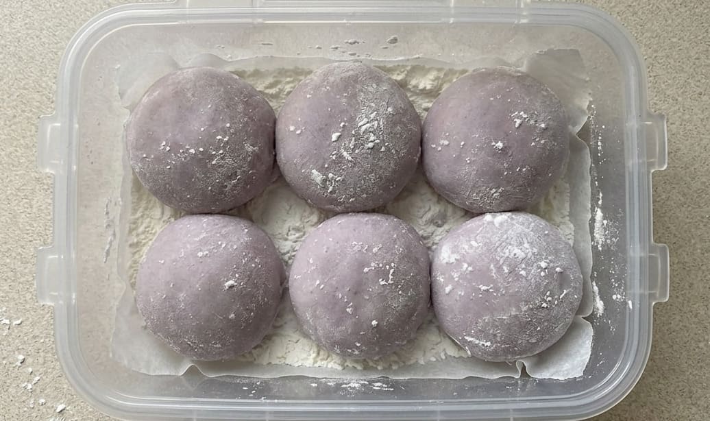Six mochis à l'ube violets rangés dans une boîte de conservation hermétique sur un lit de fécule, vue de dessus, prêts à être conservés ou transportés