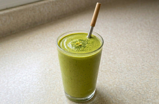 Grand verre de smoothie matcha banane crémeux de couleur vert pâle avec une paille en inox et bambou, posé sur un plan de travail en lumière naturelle