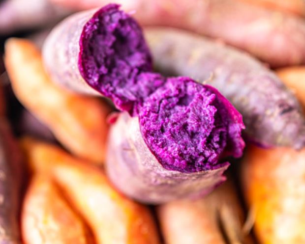 Racine d’ube violette fraîche, posée sur une planche en bois, montrant sa peau rugueuse brun-violet et sa chair violette vive typique du tubercule philippin.